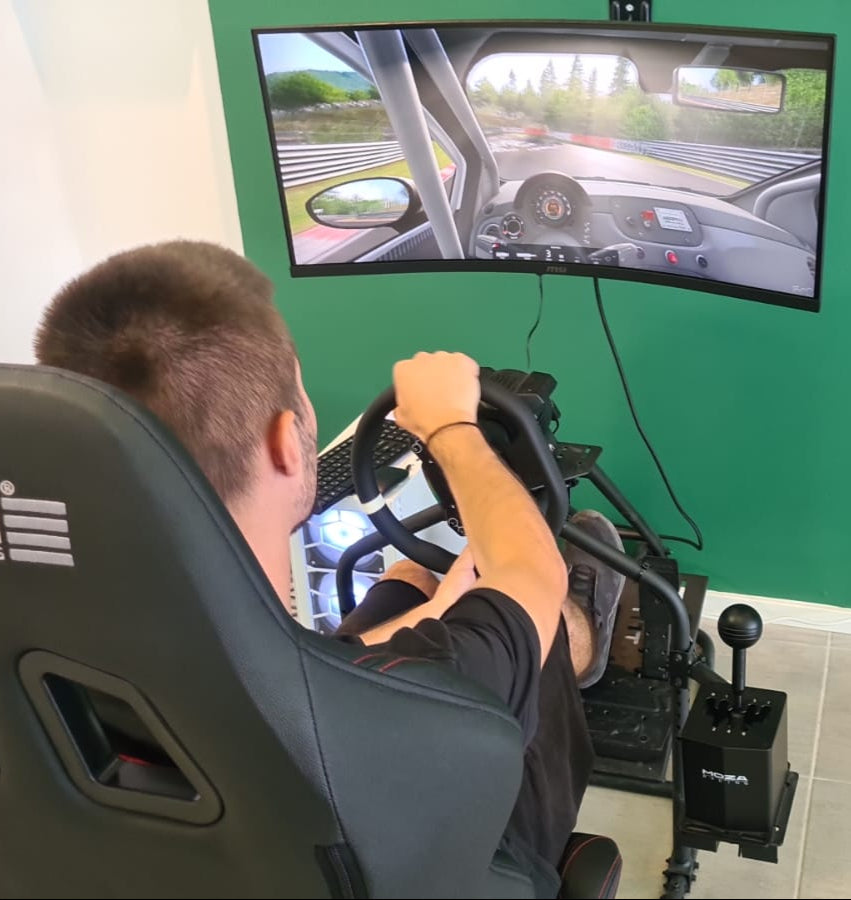 Person playing a racing game on a simulator with a green wall in the background